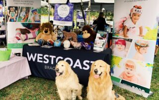 2 golden retrievers, one with a prosthetic leg, in front of WCBL table at High Risk Hope Tot Trot
