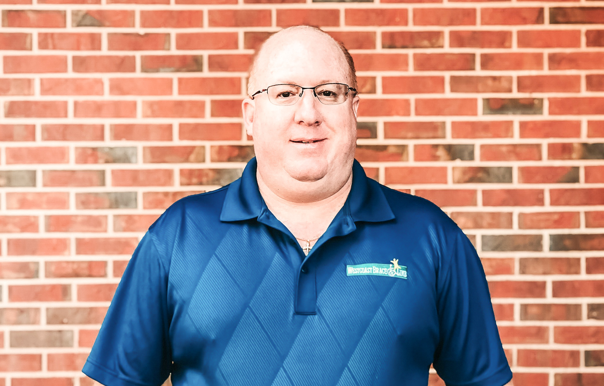 man in blue polo shirt standing in front of brick wall